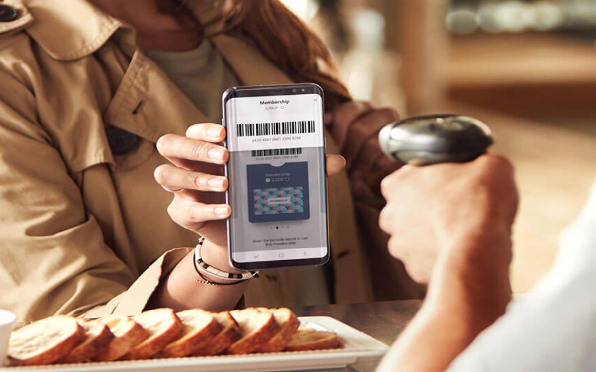 A Real Fan holding up a phone showing a TapNPay+ digital gift card barcode to be scanned at checkout